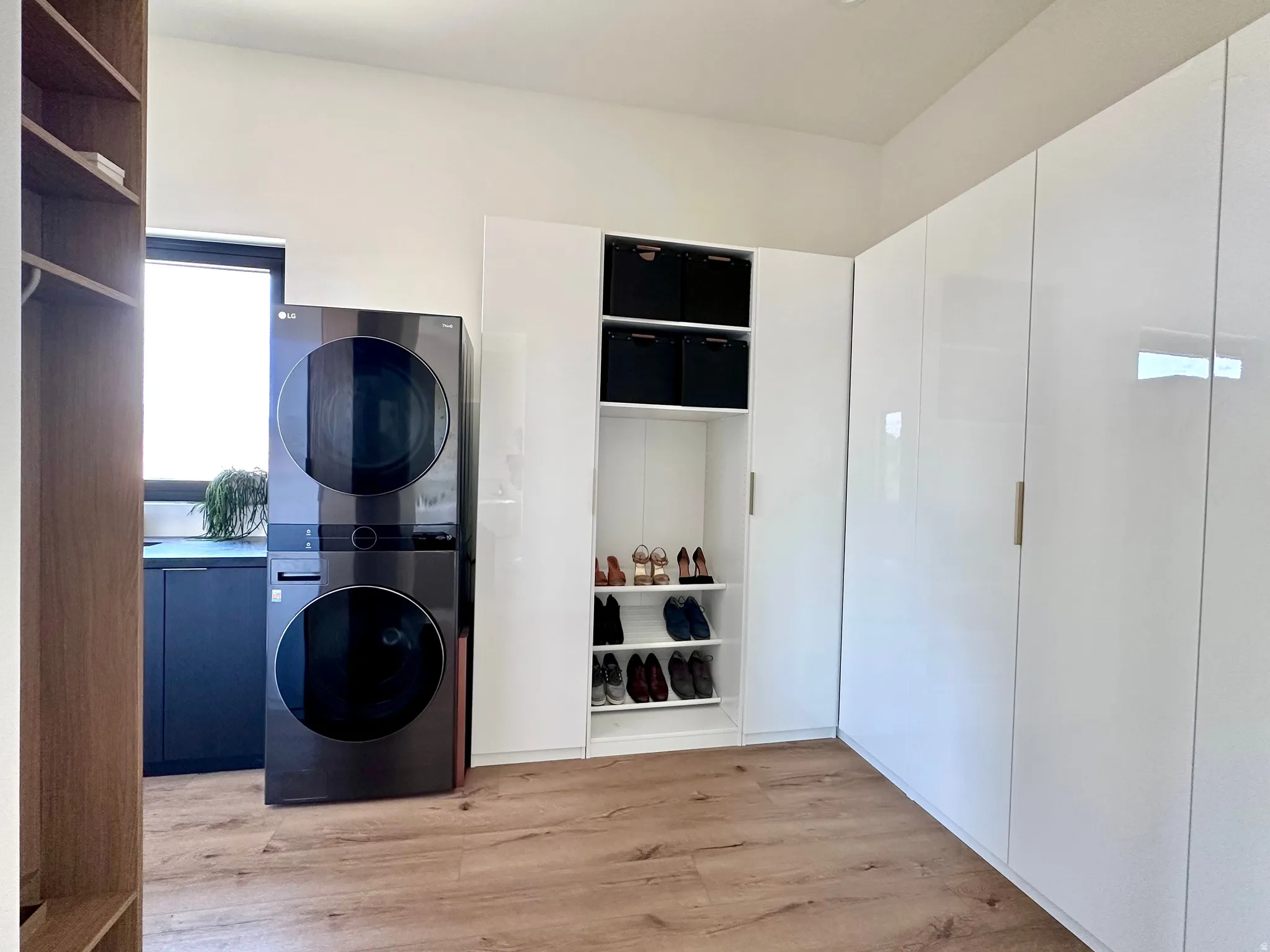 White high-gloss cabinetry, wood-finish flooring, built-in shelving, and a stacked washer and dryer