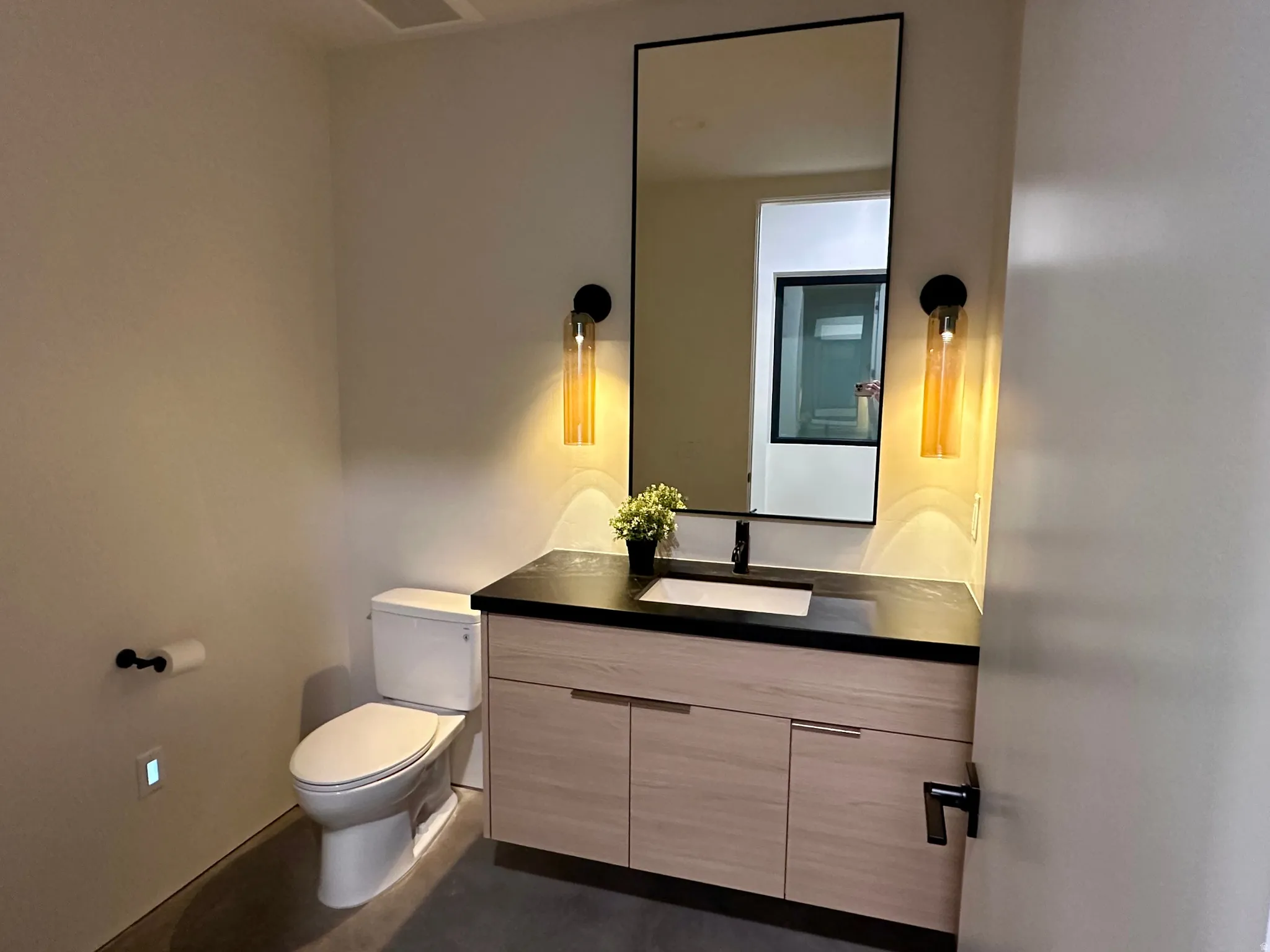 Modern vanity with wood-finish cabinetry, black countertop, and rectangular undermount sink