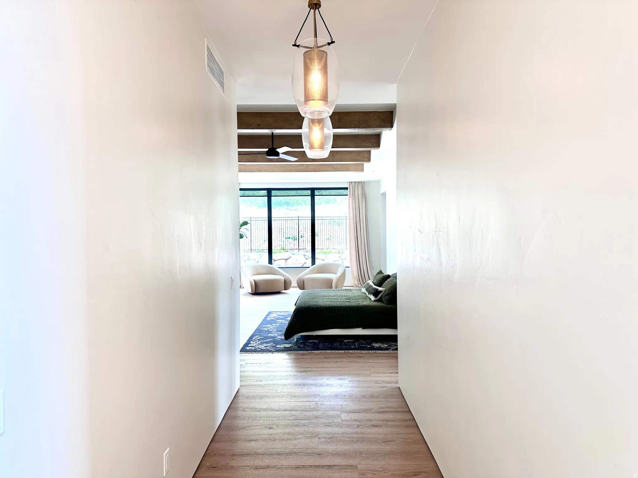 Wood-finish flooring leading to a room featuring large windows, exposed ceiling beams, and a modern ceiling fan