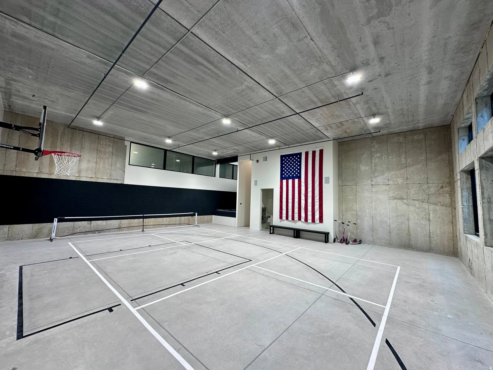 Multi-sport court with a basketball hoop, overhead lighting, and concrete walls and flooring