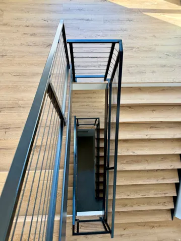 Multi-level staircase featuring wood-finish treads and risers, black metal railings, and contrasting dark wall