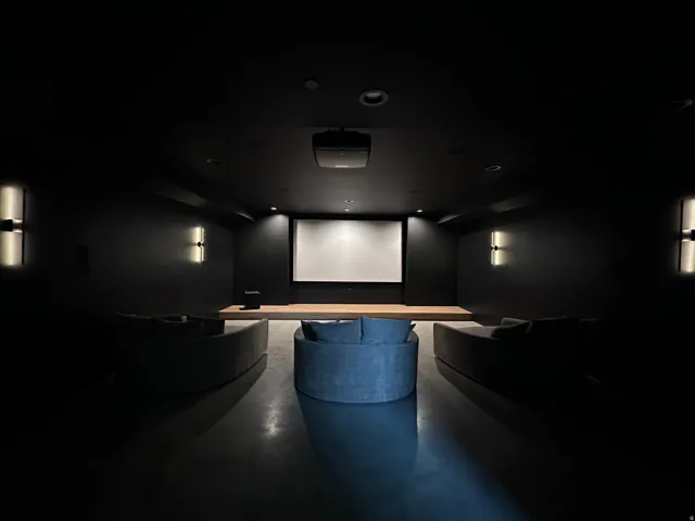 Dedicated media room featuring a large projection screen, an elevated wood-finish platform, recessed lighting, and wall-mounted sconces