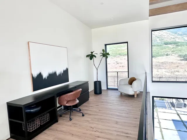 Wood-finish flooring, high ceilings, large windows with black frames, and a black metal railing