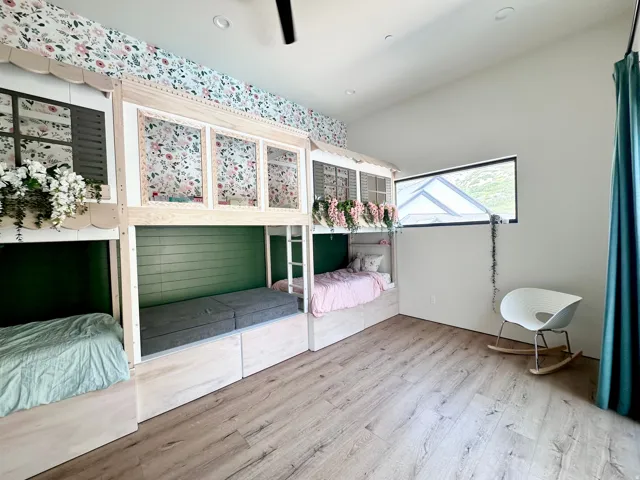 Built-in bunk beds with decorative window details, wood-finish flooring, accent wall with botanical wallpaper, and sloped ceiling