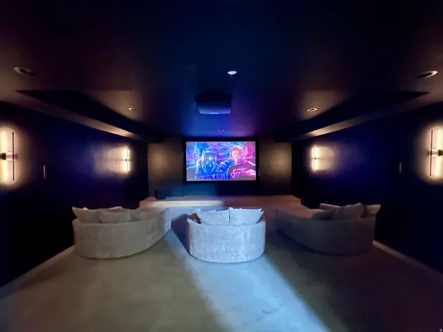 Dedicated media room featuring a large projection screen, recessed ceiling lighting, and built-in wall sconces