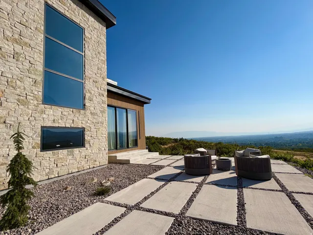 Exterior stone cladding, expansive sliding glass doors, multiple large windows, elevated outdoor patio, and gravel landscaping