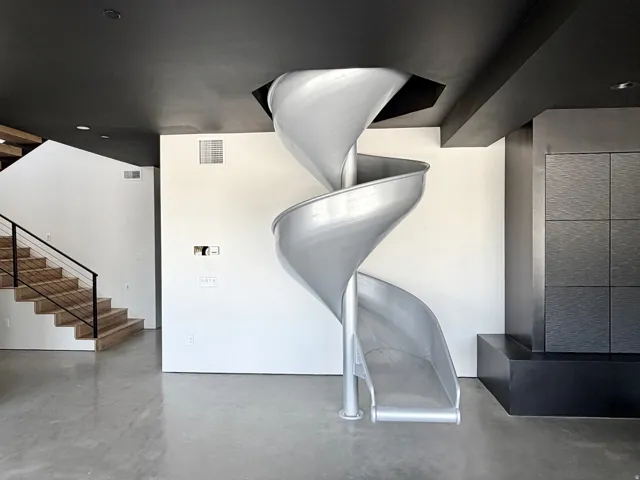 Polished concrete flooring, spiral slide, black ceiling, light wood-finish staircase with metal railing, and a dark tiled feature wall