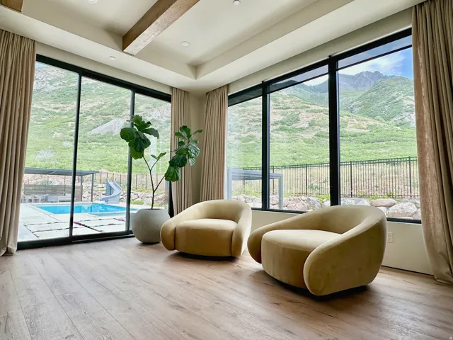 Expansive window walls, wood-finish flooring, recessed lighting, exposed ceiling beams, and a visible pool