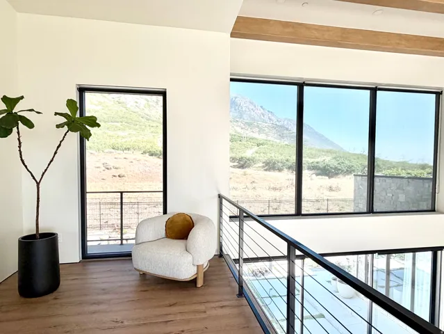 High ceilings with exposed wood beams, expansive floor-to-ceiling windows, wood-finish flooring, and a contemporary cable railing system