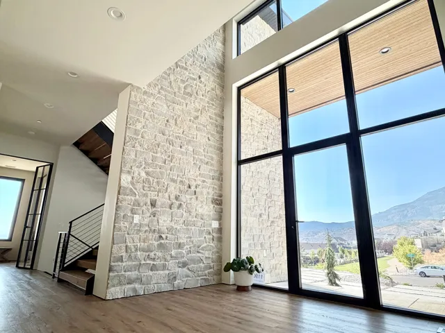 Soaring ceilings with recessed lighting, floor-to-ceiling windows, stone accent wall, wood-finish flooring, and modern staircase with cable railing