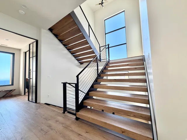 Open-tread staircase with wood-finish steps and cable railings, expansive window, wood-finish flooring, and black-framed glass doors