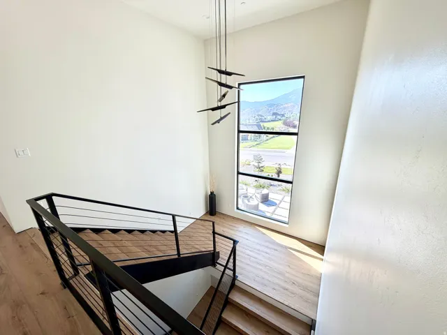 Expansive window with multi-pane design, modern staircase with black metal railing, wood-finish flooring, and contemporary pendant lighting