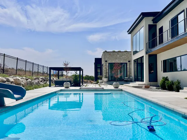 Outdoor swimming pool with integrated slide, contemporary multi-story exterior, stone-clad accent walls, large format windows, and a pergola-covered patio area