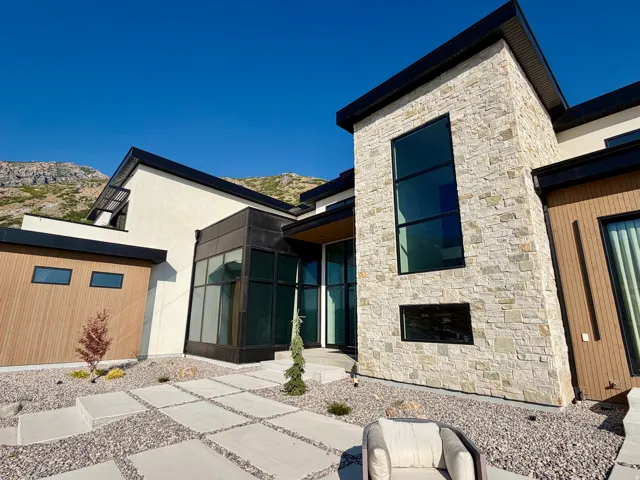 Contemporary exterior with stone facade, wood-finish siding, expansive windows, flat rooflines, and concrete paver walkway