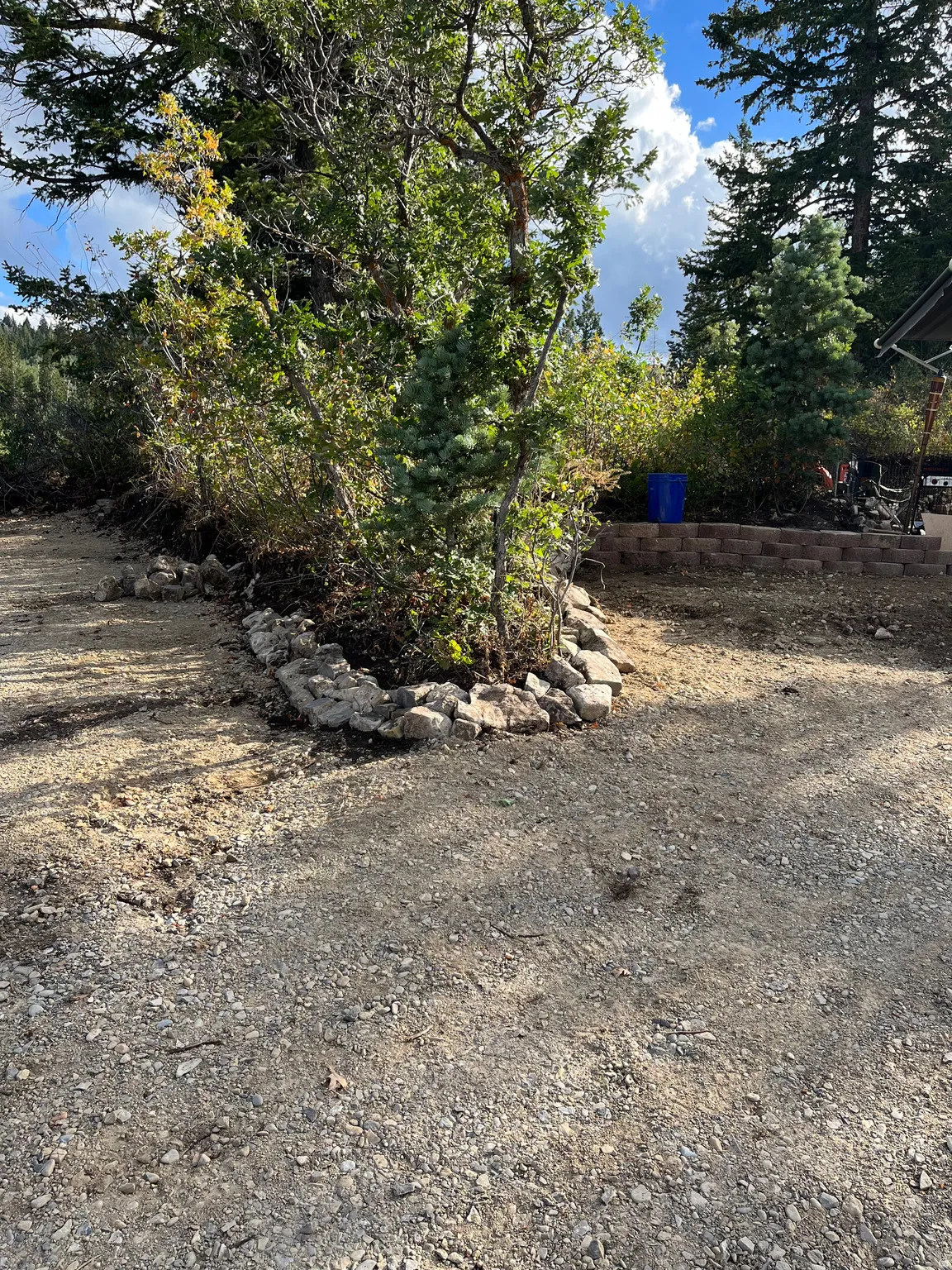 Gravel ground cover with a rock-lined planting area featuring mature trees and shrubs