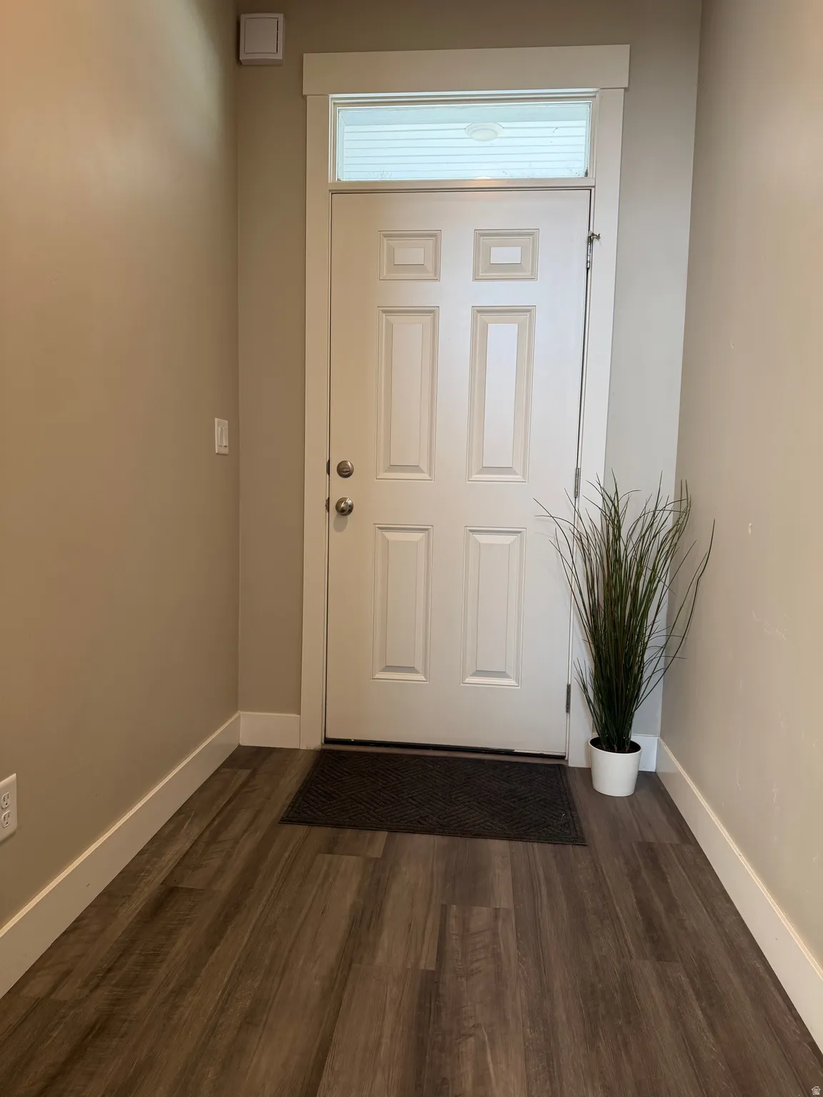 Entryway featuring wood-finish flooring, a white paneled door with a transom window, and neutral wall tones