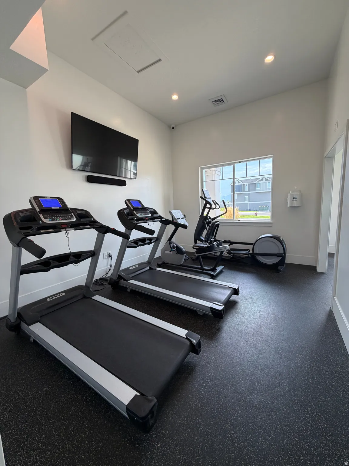 Recessed ceiling lighting, wall-mounted television, soundbar, rubberized flooring, and a large window
