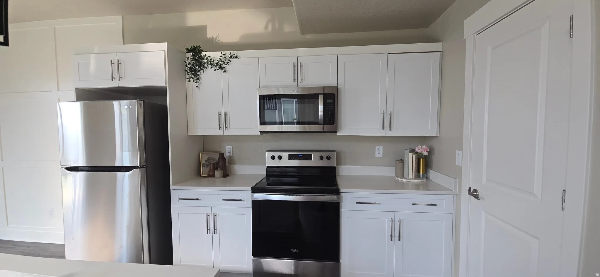 Modern kitchen featuring white shaker cabinetry, stainless steel appliances, light-toned countertops, a built-in microwave, and a paneled refrigerator surround