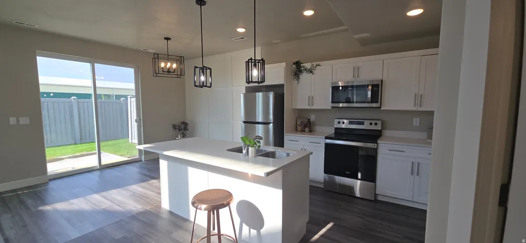 Open-concept kitchen featuring an island with an integrated sink, white cabinetry, and stainless steel appliances