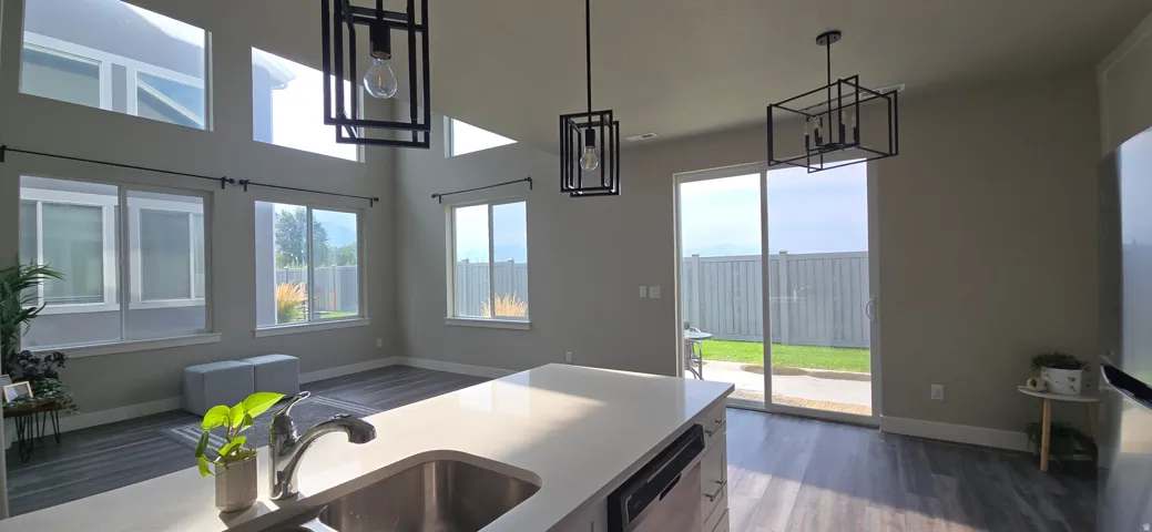 Vaulted ceilings with clerestory windows, modern pendant lighting, wood-finish flooring, and a sliding glass door to the backyard