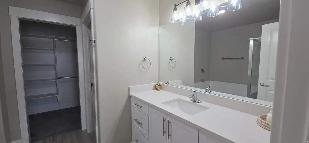 Spacious bathroom featuring a white vanity with integrated sink, large mirror, and contemporary light fixture