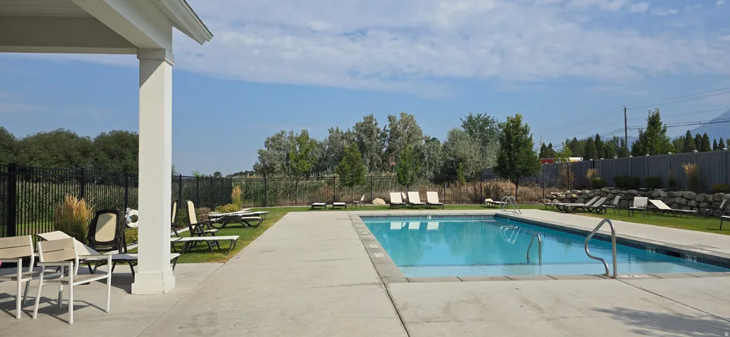 Outdoor pool with concrete decking, surrounded by a black metal fence and mature landscaping