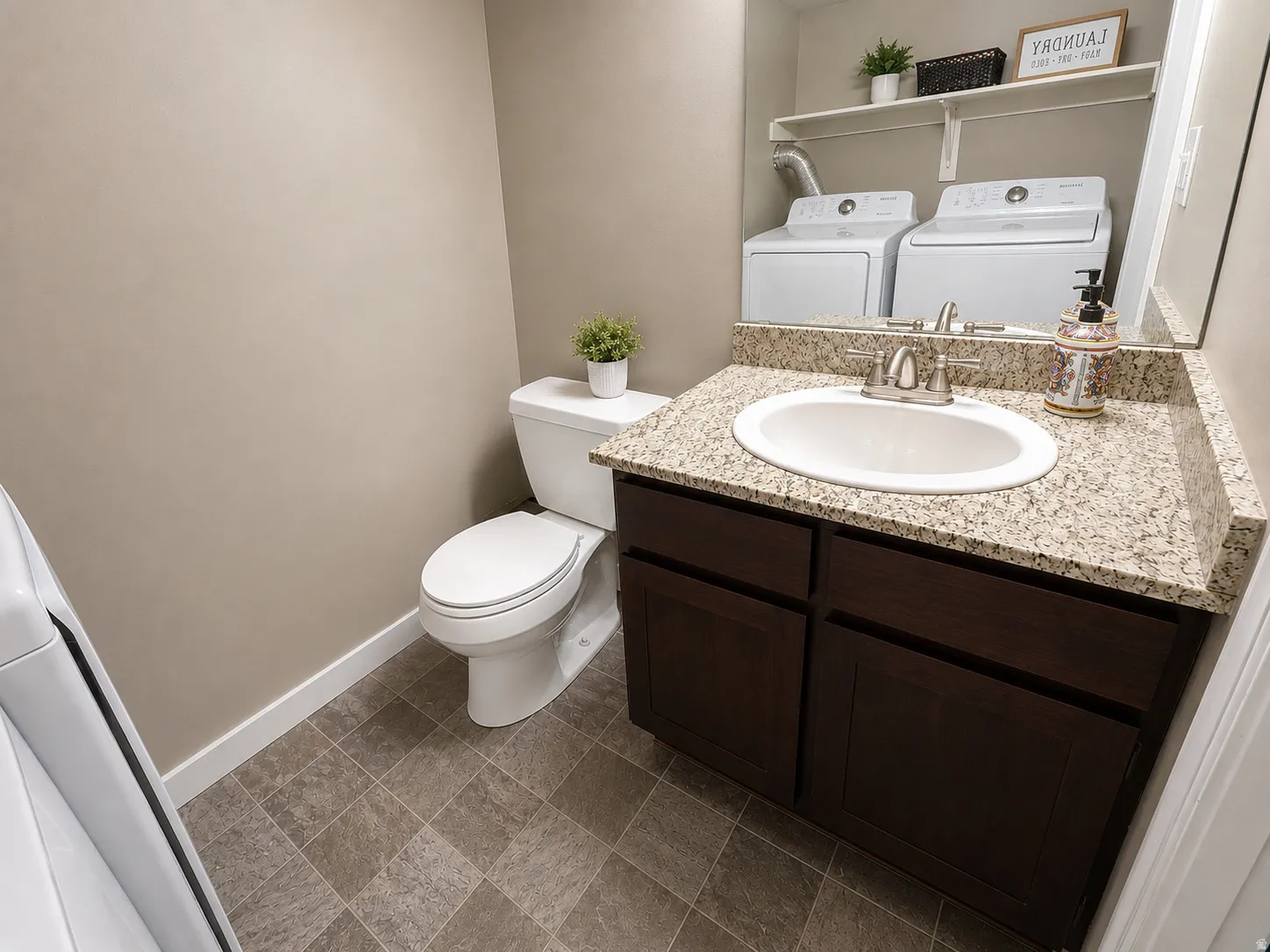 Vanity with a granite-style countertop and undermount sink, dark wood-finish cabinetry, and tiled flooring