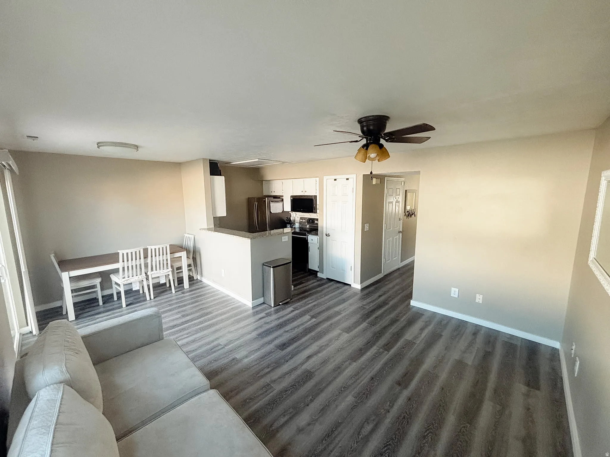 Spacious open-concept living area featuring wood-finish flooring, a kitchen island with a breakfast bar, and a ceiling fan with integrated lighting