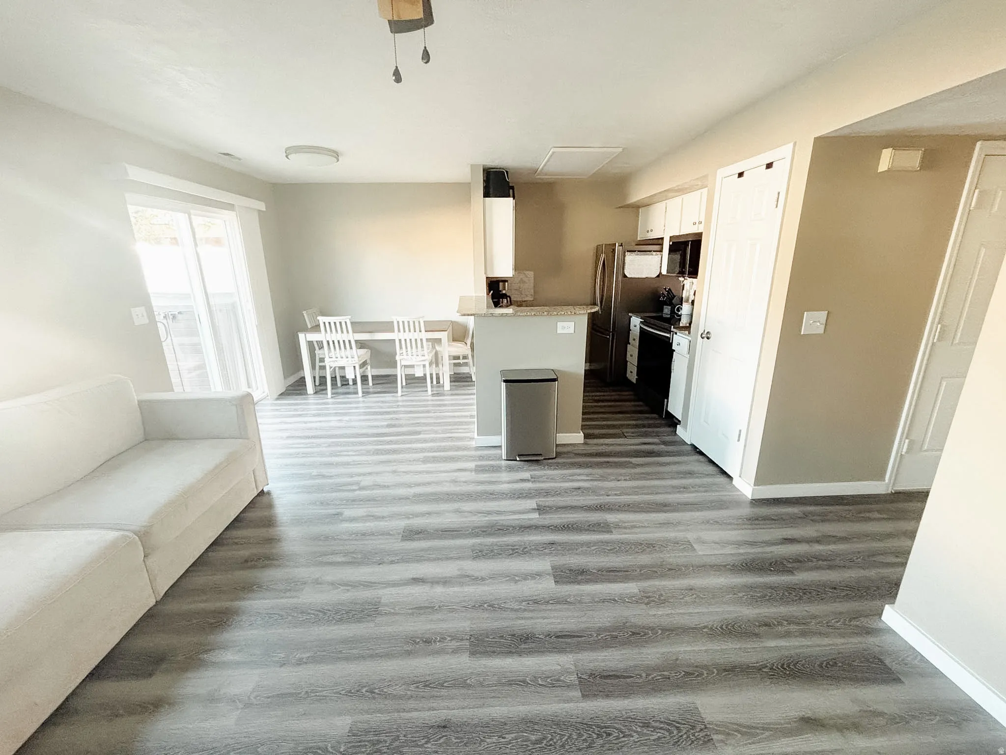 Open-concept room featuring wood-finish flooring, sliding glass door, and a kitchen with white cabinetry and stainless steel appliances