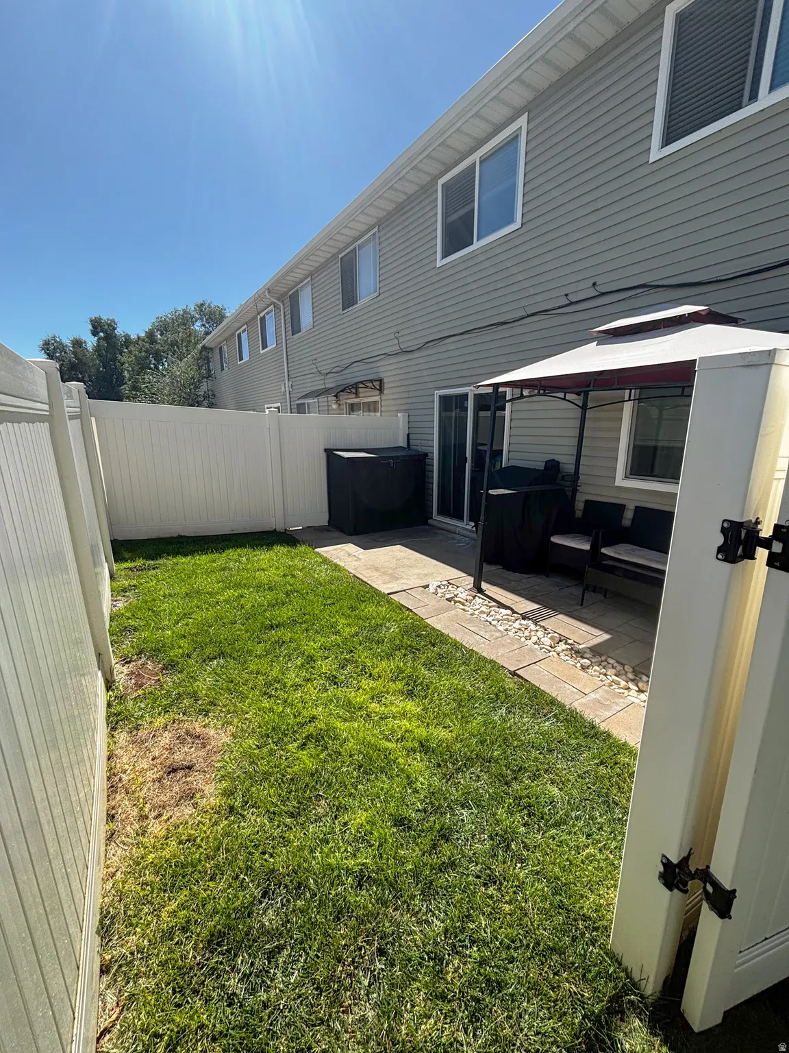 Fenced backyard featuring a paved patio area, green lawn, and sliding glass door access