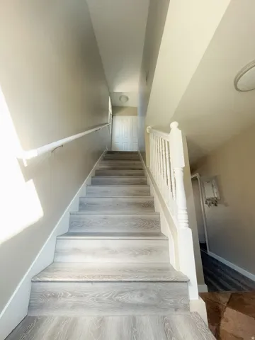 Staircase featuring wood-finish treads and risers, a painted handrail, and a white spindle banister