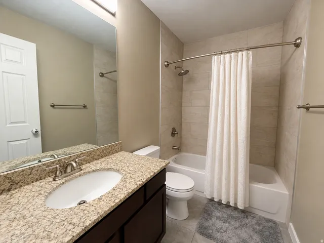 Granite-look countertop with an undermount sink, dark wood-finish vanity, tiled shower surround, and brushed nickel fixtures
