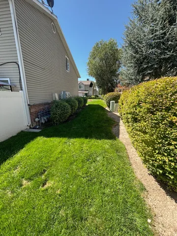 Side yard with manicured lawn, established shrubs, and a privacy fence