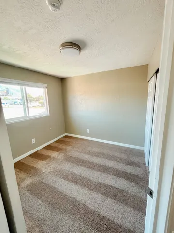 Wall-to-wall carpeting, neutral wall colors, flush-mount ceiling light, window with white trim, and bi-fold closet doors