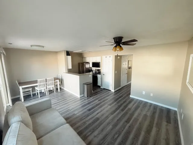 Spacious open-concept living area featuring wood-finish flooring, a kitchen island with a breakfast bar, and a ceiling fan with integrated lighting