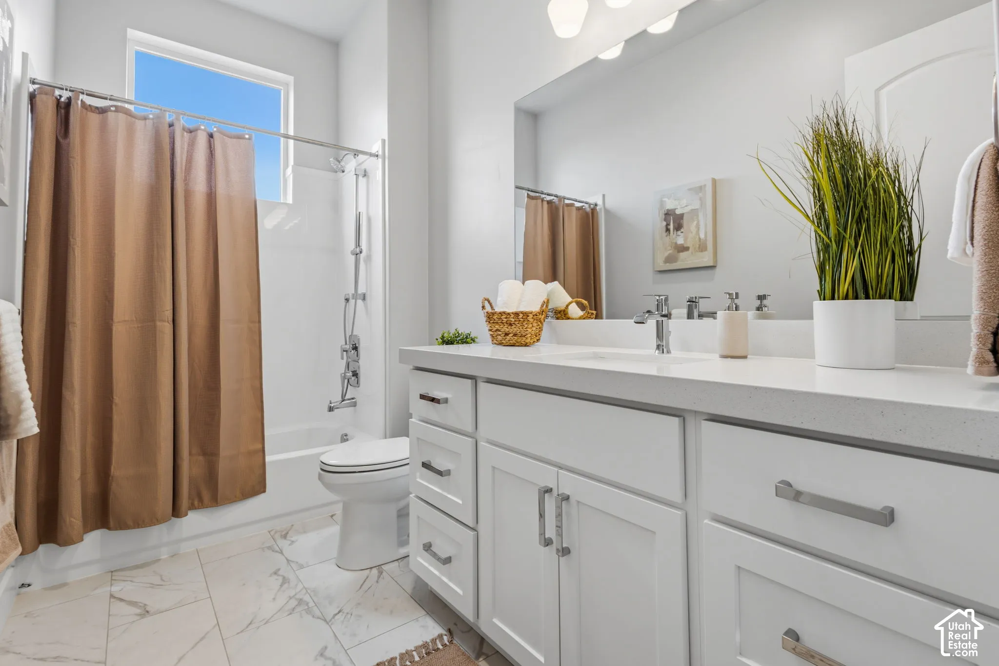 White cabinetry with brushed nickel hardware, expansive vanity countertop, integrated sink, large wall-mounted mirror, and tile flooring