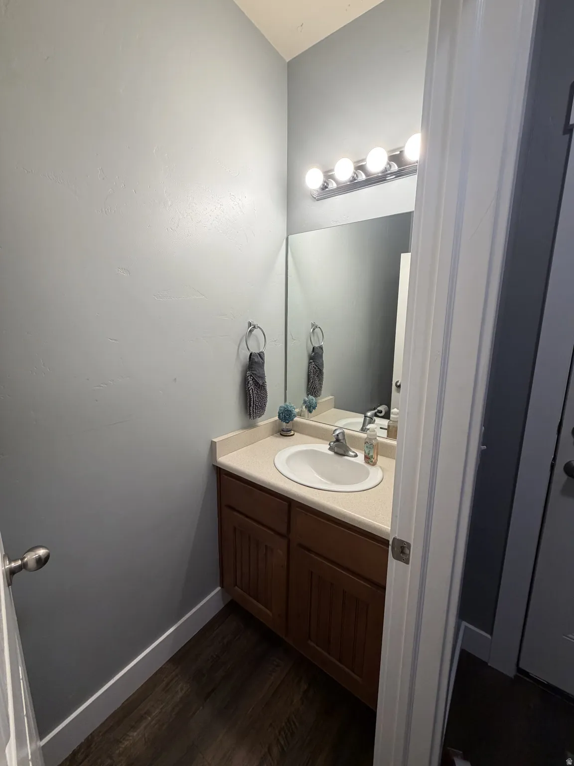 Bathroom featuring a wood-finish vanity with ample storage, white porcelain sink, and quartz countertop