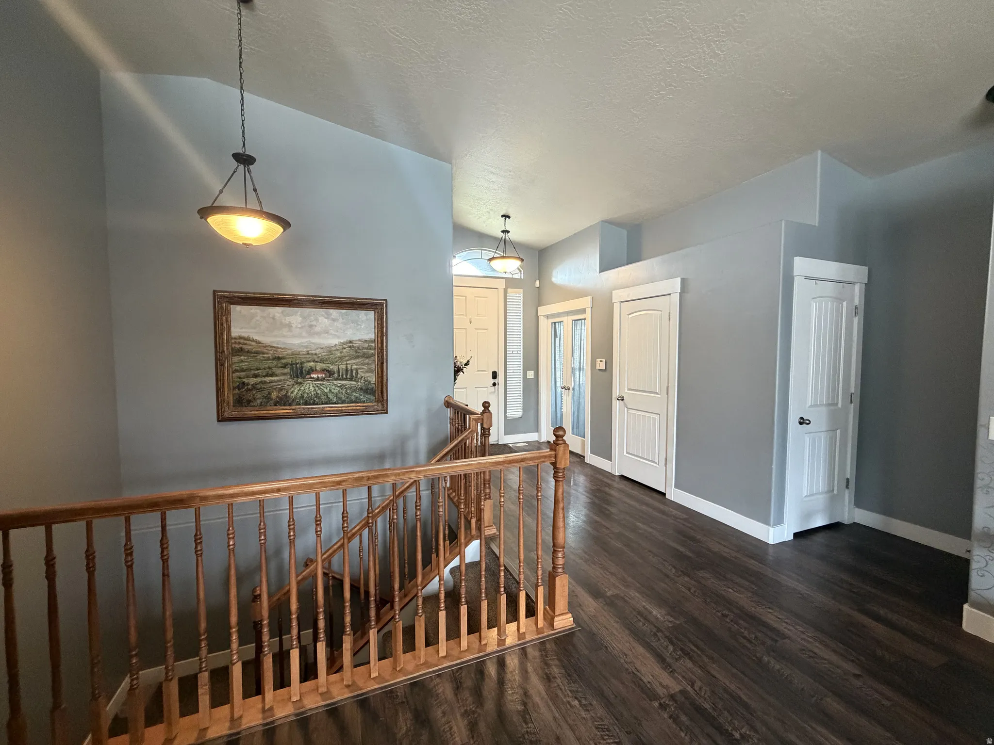 Vaulted ceiling, wood-finish flooring, wood staircase with balusters, two panel doors, and a full-light French door