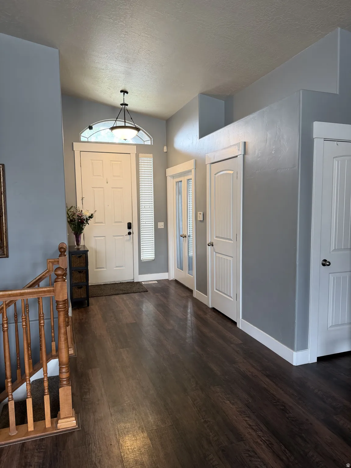 Welcoming foyer showcasing dark wood-finish flooring, soft overhead pendant lighting, and clean white six-panel doors