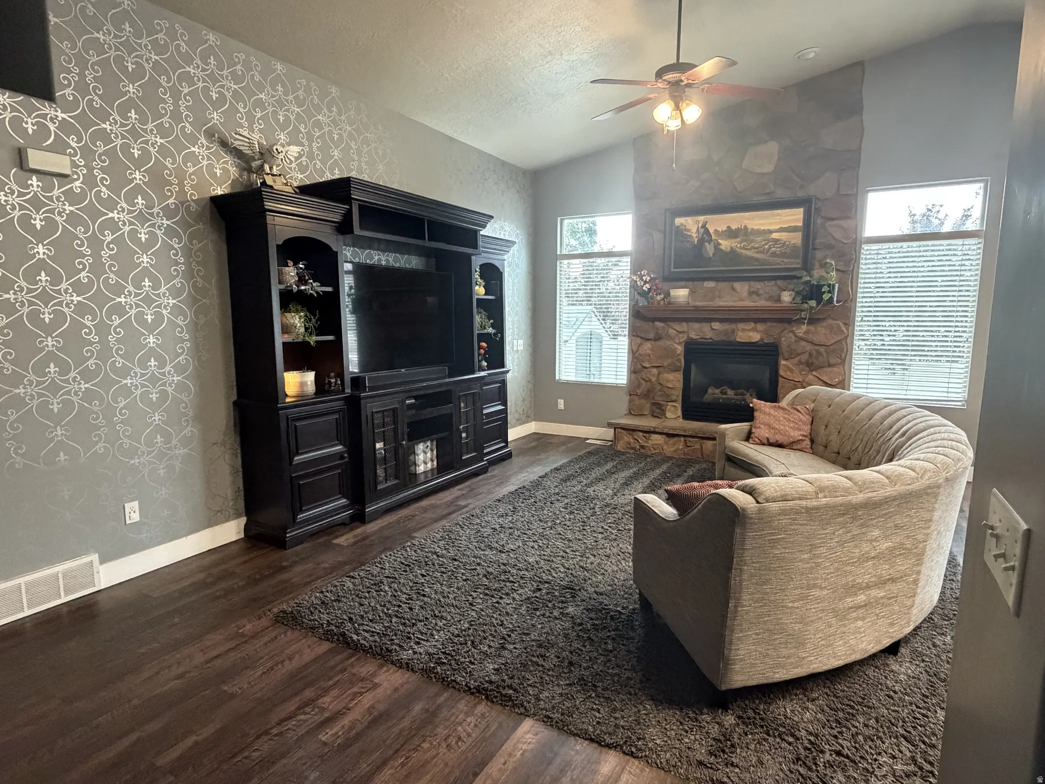 Spacious living room featuring a wood-finish plank floor, geometric-patterned accent wall, and a brick fireplace with mantel