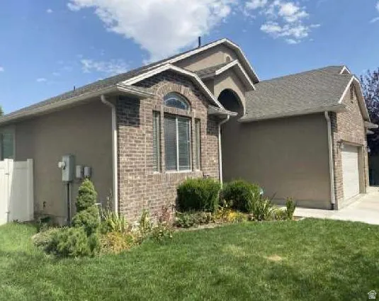 Exterior featuring brick and stucco finishes, arched window, attached garage, and landscaping