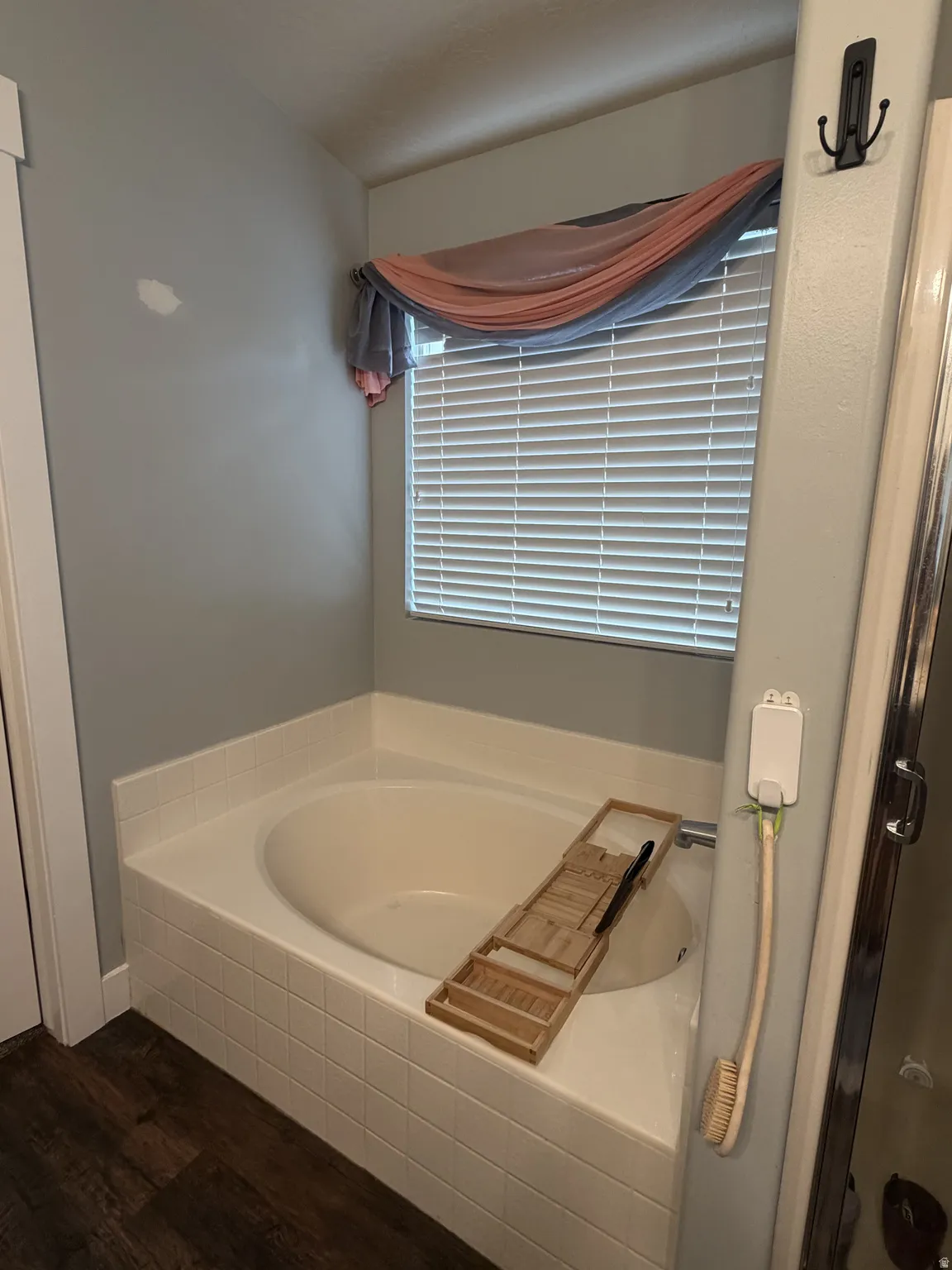 Primary suite #1. Soaking tub with integrated surround and tile detailing, complemented by a large window with horizontal blinds and natural light