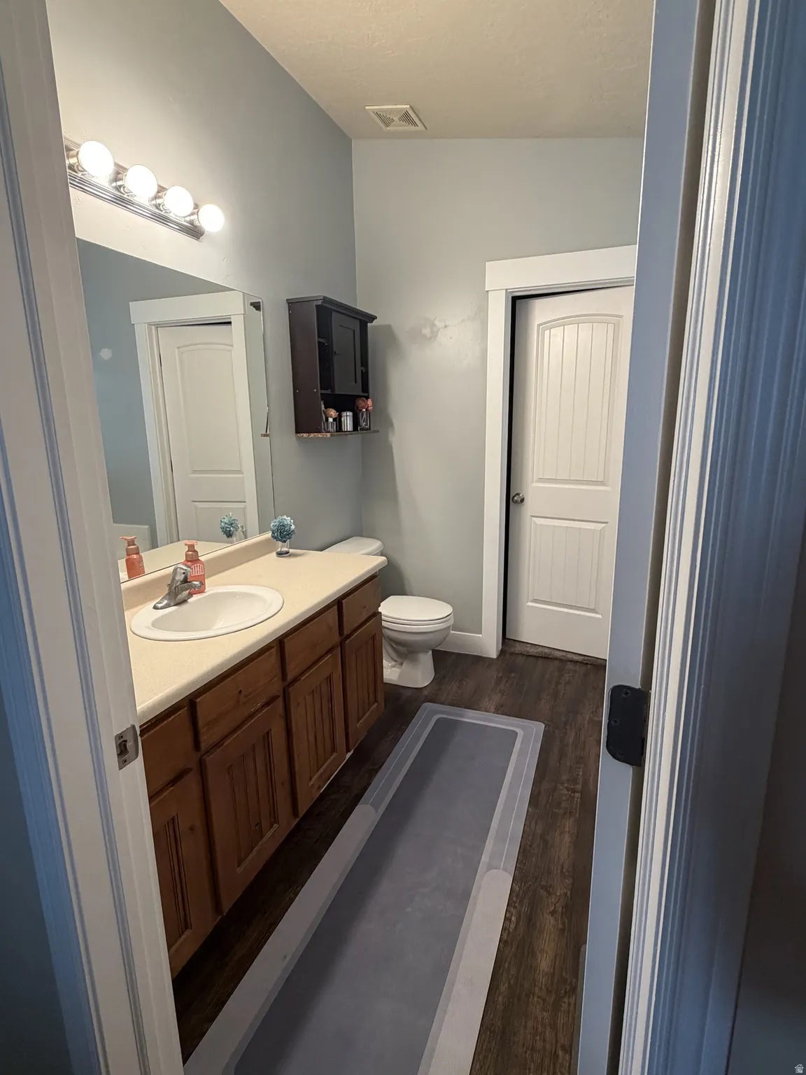 Primary suite #1 bath. Dual vanity bathroom with wood-finish cabinetry, ceramic sink fixtures, and abundant overhead lighting