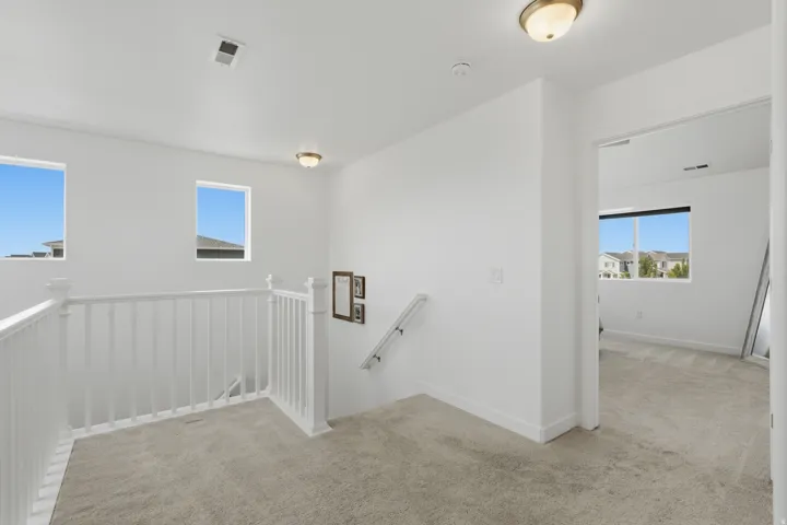Carpeted hallway with white walls, multiple windows, white railing, and flush-mount lighting fixtures