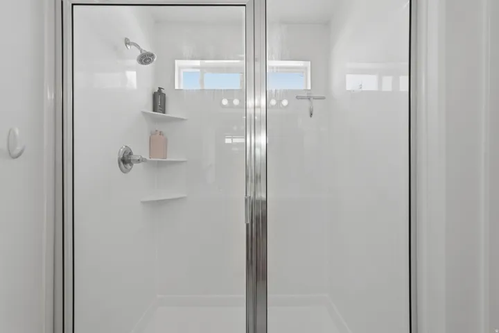 Glass-enclosed shower with a chrome shower head and built-in shelving