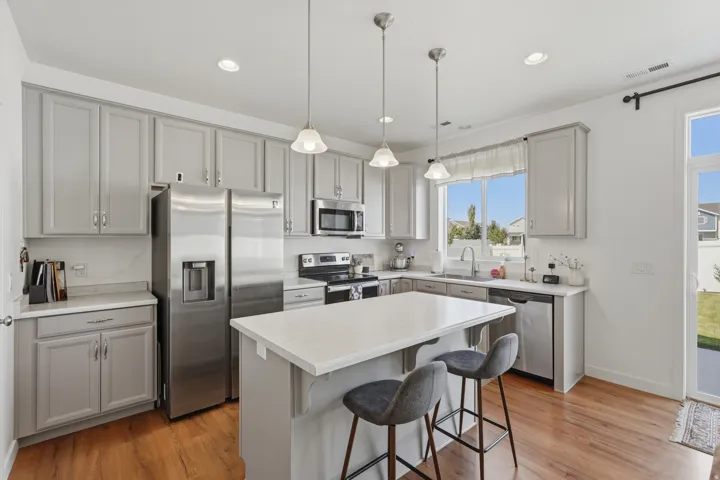 Spacious kitchen featuring gray shaker-style cabinetry, a central island with a light-toned countertop, stainless steel appliances, and wood-finish flooring