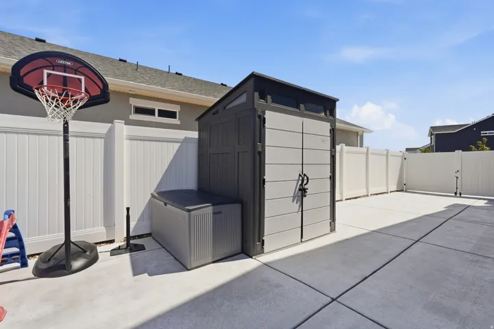 Paved patio with a storage shed, white privacy fencing, and an access gate