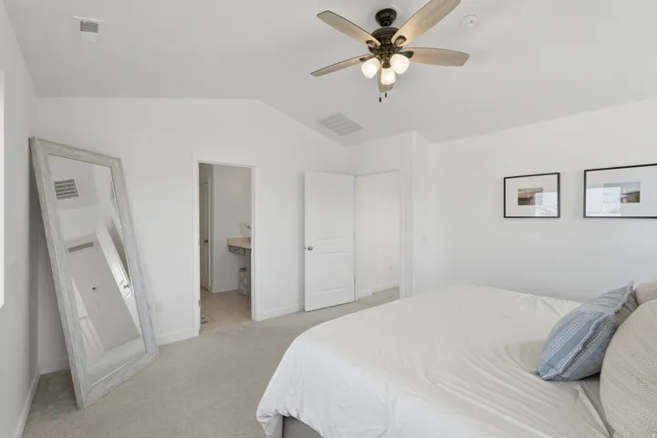Vaulted ceiling with a ceiling fan light fixture, light-toned carpet flooring, white painted walls, and a doorway opening to an additional space