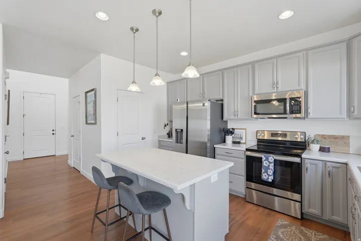 Kitchen featuring light gray cabinetry, stainless steel appliances, white countertops, a center island with pendant lighting, and wood-finish flooring