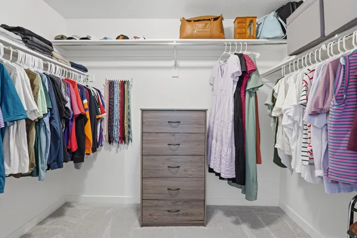 Walk-in closet featuring white wire shelving, multiple hanging rods, and a standalone five-drawer dresser
